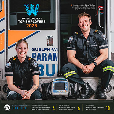 Two smiling paramedics, a woman and a man, are sitting in front of an ambulance labeled 